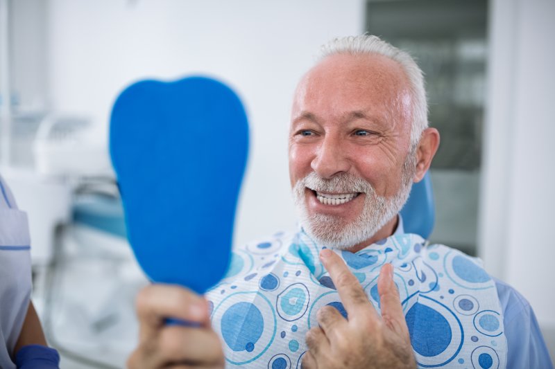 an older man smiling at himself in the mirror at the dentist office